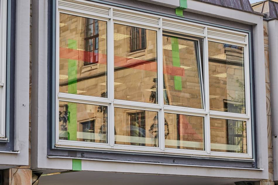 Rote und grüne Folien und Bleche ziehen sich innen wie außen an einem großen Fenster des Gebäudes der Osnabrücker Stadtbibliothek entlang.