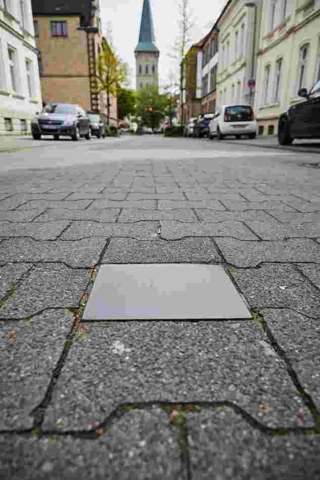 Eine Stahlplatte, die in der Mitte der Straße eingelassen ist. Im Hintergund in der Ferne ist ein Kirchenturm.