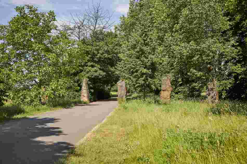 5 Große Quader aus Sandstein, die den Weg kreuzen. Am Rande des Weges stehen Bäume.