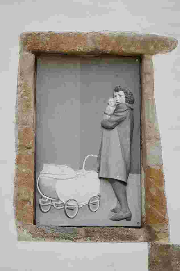 Gedenkrelief von Heinrich und Jacob Brummack: Eine Frau mit einem Baby auf ihrem Arm. Sie blickt über ihre Schulter in die Ferne. Neben ihr steht ein Kinderwagen.