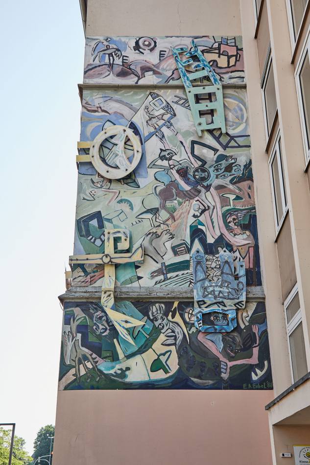 Ein großes Wandbild, das in 3 Teile geteilt ist. Sie sehen aus wie Himmel, Erde und Hölle. Auf dem Bild gibt es viele verschiedene Formen, Farben und Figuren. Manche sehen aus wie Menschen, andere wie Tiere. Das Bild ist wie ein riesiges Wimmelbild.