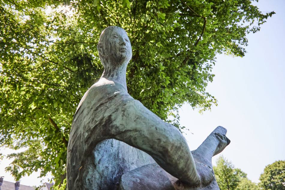 Eine männliche Figur aus Bronze sitzt auf einem Sockel und spielt die Laute.