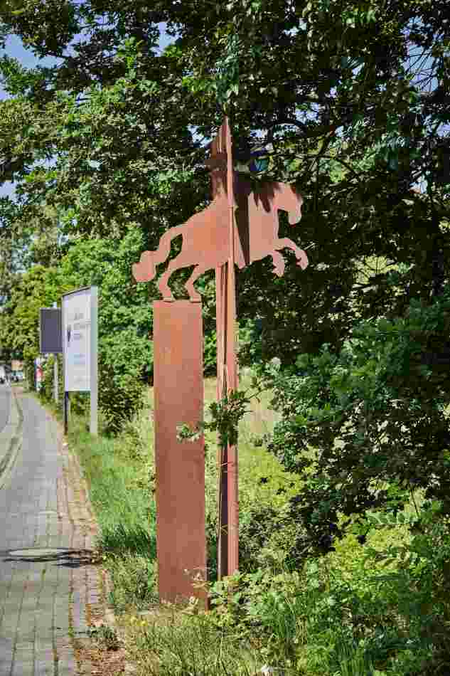 Am Rand eines Weges, unter einem Baum steht Skulptur 