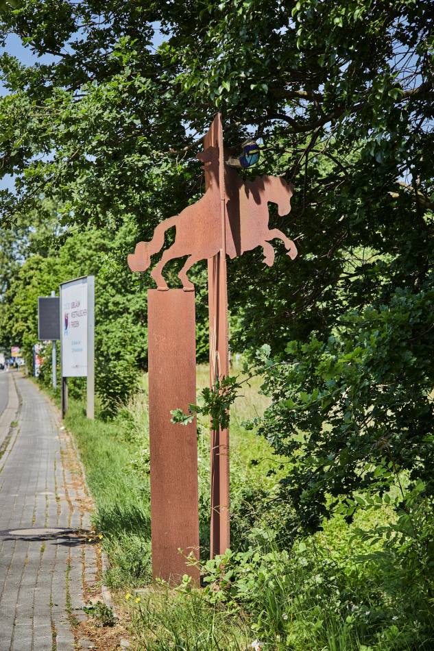 Am Rand eines Weges, unter einem Baum steht Skulptur 