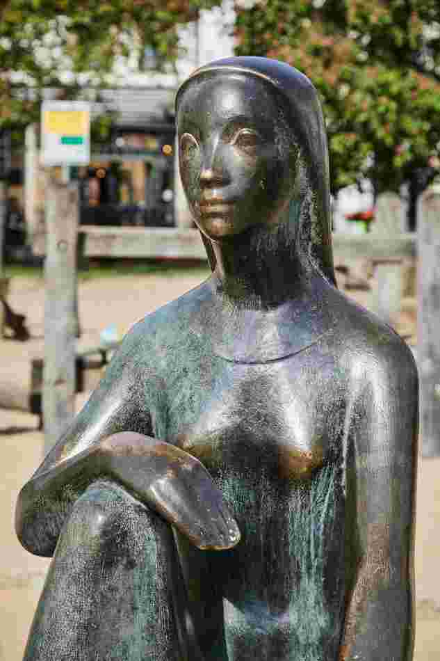 Eine kleine weibliche Figur aus Bronze sitzt in einer entspannten Haltung. Die Figur hat eine einfache Formensprache.