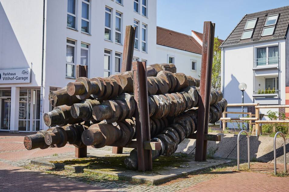 Vor einem Parkhaus steht die Skulptur „Time is turning“:  Auf mehreren Stahlträgern sind 11 Schiffskurbelwellen aus massivem Stahl angeordnet.